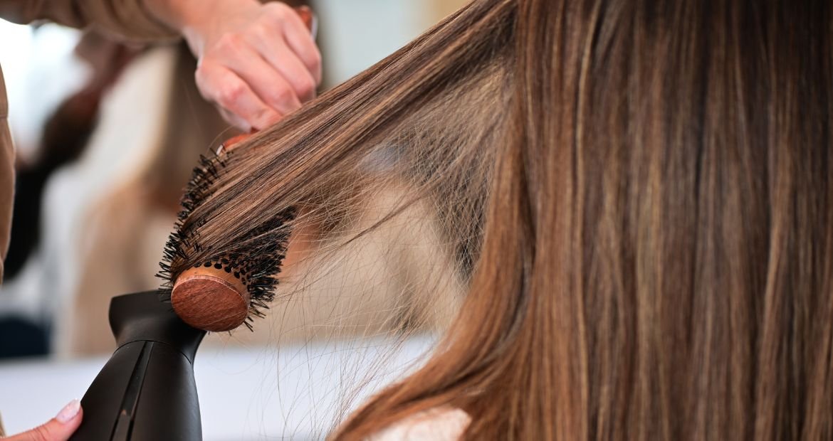 Profissional secando o cabelo de uma jovem com secador após usar o protetor térmico para proteger os fios.